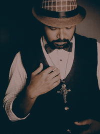 Portrait of young man holding hat against black background