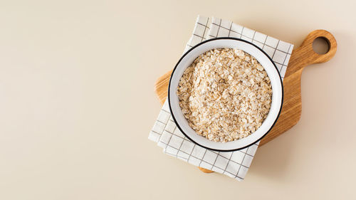 Oat flakes in a bowl on a napkin on a beige background. copy space.