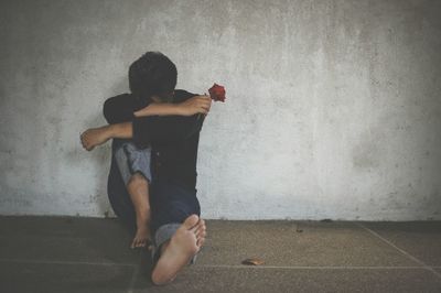 Sad man holding rose sitting against wall