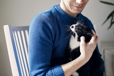 Young man stroking his cat at home during sunny day. 