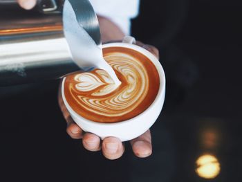 Close-up of hand pouring milk in coffee cup