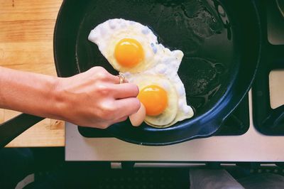 Cropped hand of woman cooking omelet in pan on stove