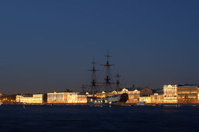 Sailboats in sea by illuminated buildings against clear sky at night