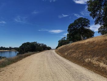 Dirt road by trees against sky