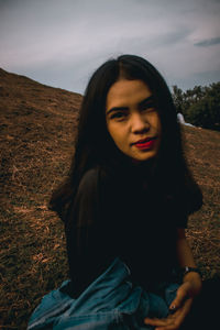 Portrait of young woman sitting on field against sky