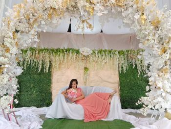 Full length of young woman holding bouquet while relaxing on sofa during wedding ceremony