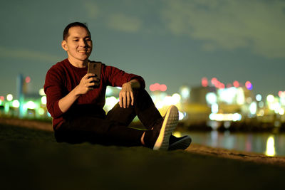 Smiling man using mobile phone in illuminated city against sky at night