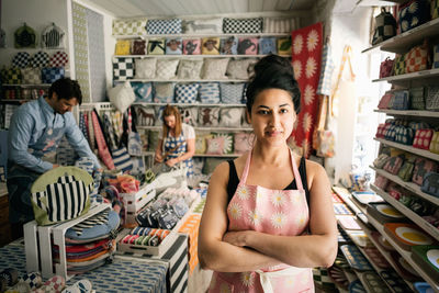 Portrait of confident owner standing with arms crossed while colleagues working in shop