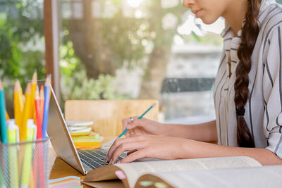 Midsection of woman studying while using laptop on table