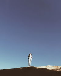 Low angle view of woman standing on desert against clear blue sky