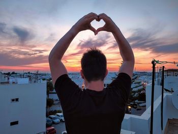 Rear view of man standing in sea against sunset sky