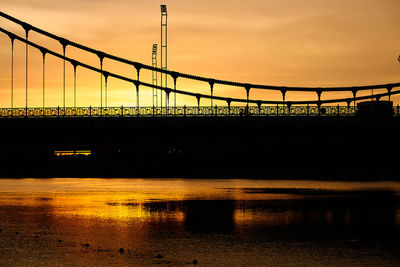 Silhouette bridge over river against sky during sunset