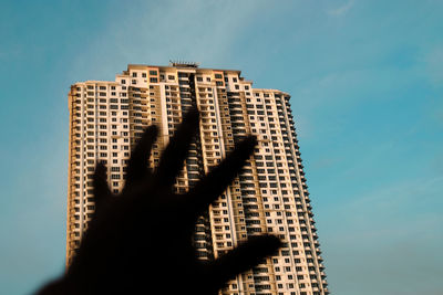 Low angle view of hand against building against sky