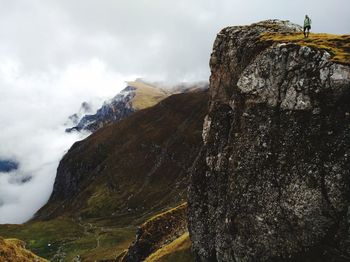 Low angle view of young woman standing on mountain against cloudy sky