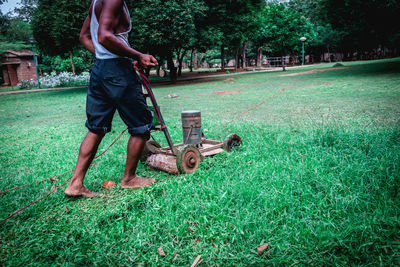 Low section of man cutting grass on field using lawn mower