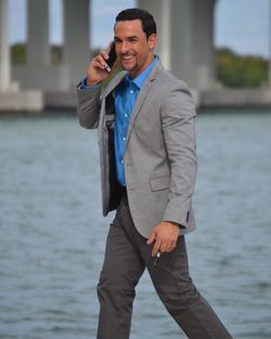 Smiling man in suit using mobile phone against lake