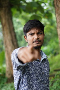 Portrait of young man standing against trees
