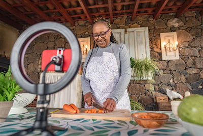 Black woman with glasses teaches online with her mobile phone cooking classes from home