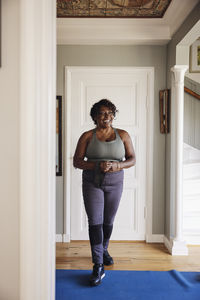 Happy woman with resistance band walking on exercise mat at home