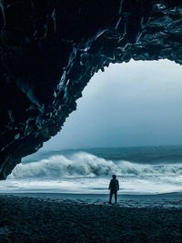 Silhouette man standing in cave at beach against sky