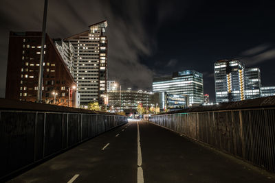 Illuminated road amidst buildings in city against sky at night