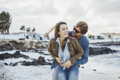 Smiling man embracing woman from behind at beach