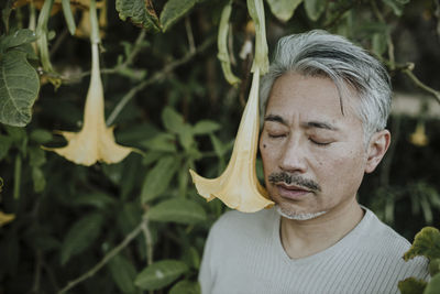 Mature man with eyes closed standing by yellow flower