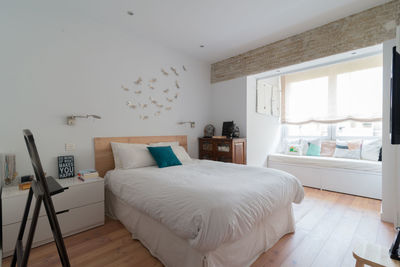 Beautiful bedroom in white with natural light, wooden floor and a sofa