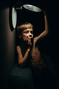 Portrait of boy standing under illuminated light at home