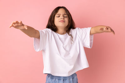 Portrait of young woman standing against pink background