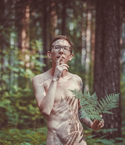 Midsection of shirtless man standing by tree in forest