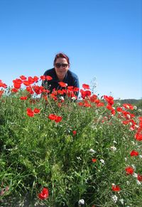 Portrait of woman bending at poppy flower field against clear sky