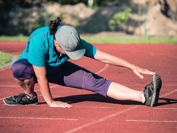 Athletic middle aged woman stretching on red running track before training, healthy fitness life