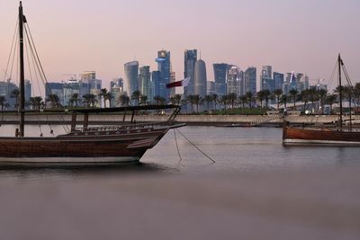 Sailboats moored on river by buildings in city against sky