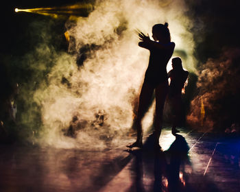 Silhouette of a woman dancing between lights and smoke unrecognozible person