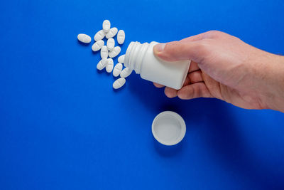 Cropped hand holding pills against blue background