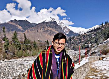 Portrait of smiling young man standing against mountains and sky