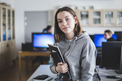 Portrait of confident high school female student with books in classroom