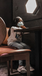 Low angle view of girl wearing mask sitting in cafe