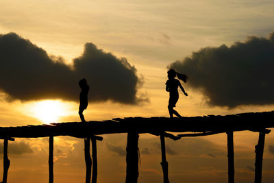 Silhouette girls on footbridge against sky during sunset