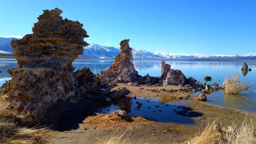 Rock formations in lake against clear blue sky