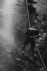 Rear view of man climbing on mountain by waterfall