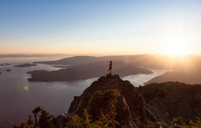 Man standing on rock against sky during sunset