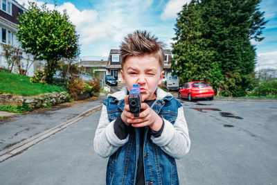 Portrait of boy shooting with toy handgun while standing on road