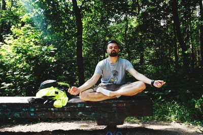 Young man sitting on tree against plants