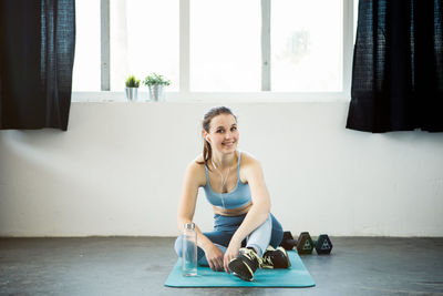 Full length of smiling young woman sitting on floor