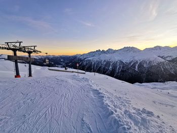 Snow covered landscape against sky during sunset