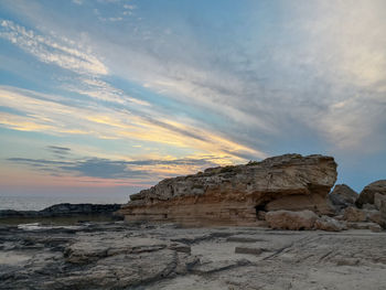 Rock formation on beach against sky during sunset