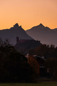 Scenic view of silhouette houses and mountains against orange sky