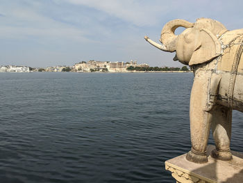 Statue of elephant by lake pichola seen from  against sky in city